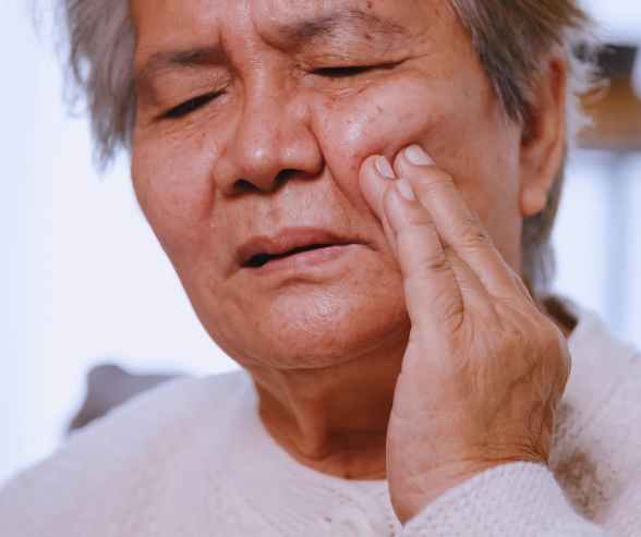An older woman rests her hand on her cheek, appearing thoughtful and contemplative.